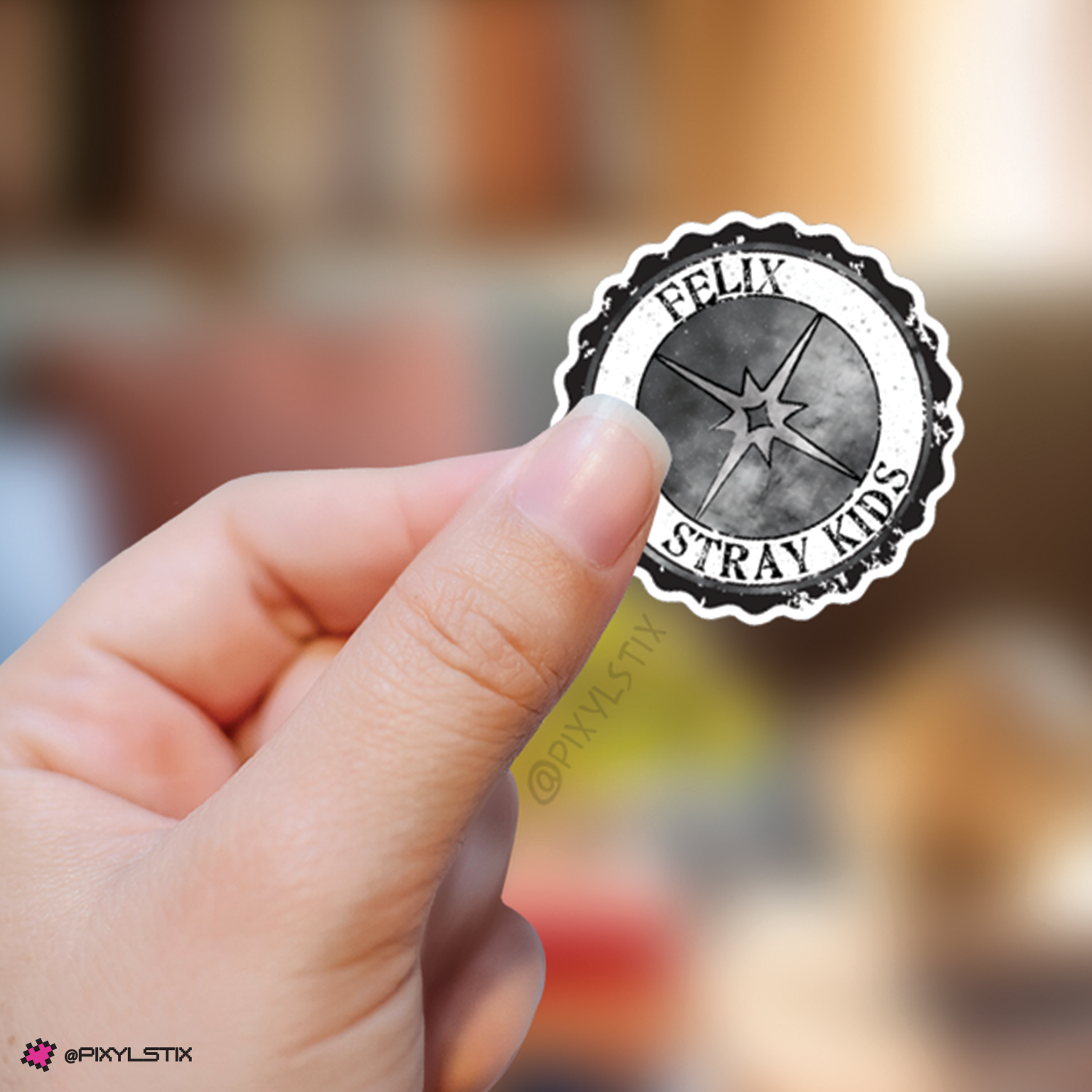 Hand holding a sticker with 'Felix Stray Kids' logo against a blurred background