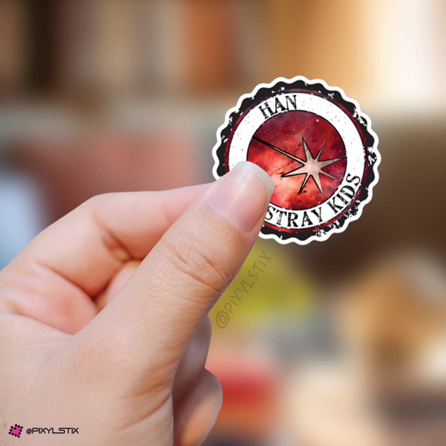 Hand holding a sticker with 'Han Stray Kids' logo against a blurred background