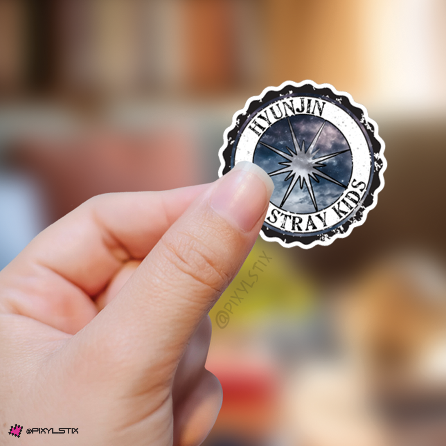 Hand holding a sticker with 'Hyunjin Stray Kids' logo against a blurred background