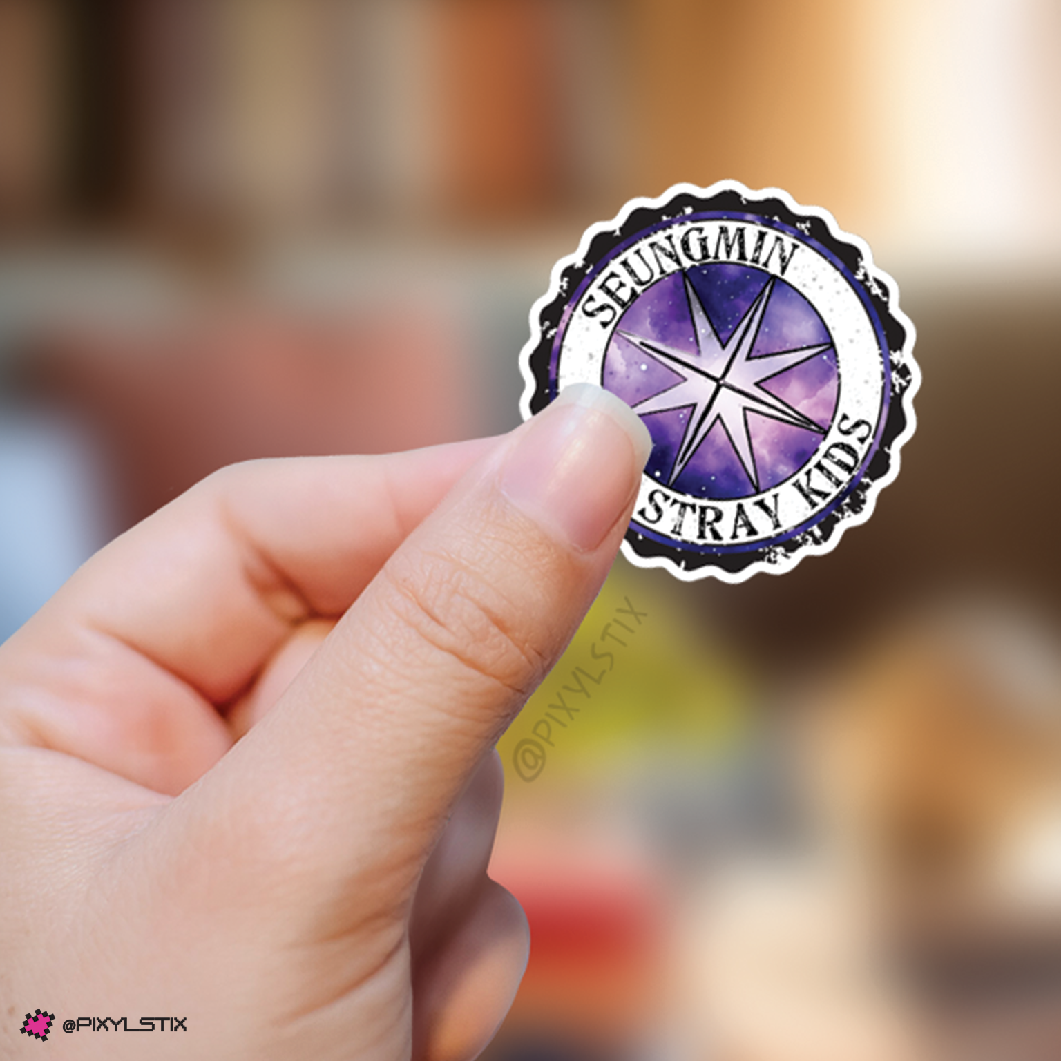 Hand holding a sticker with 'Seungmin Stray Kids' logo against a blurred background