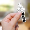 Hand holding a small black and white sticker with a design on a blurred background