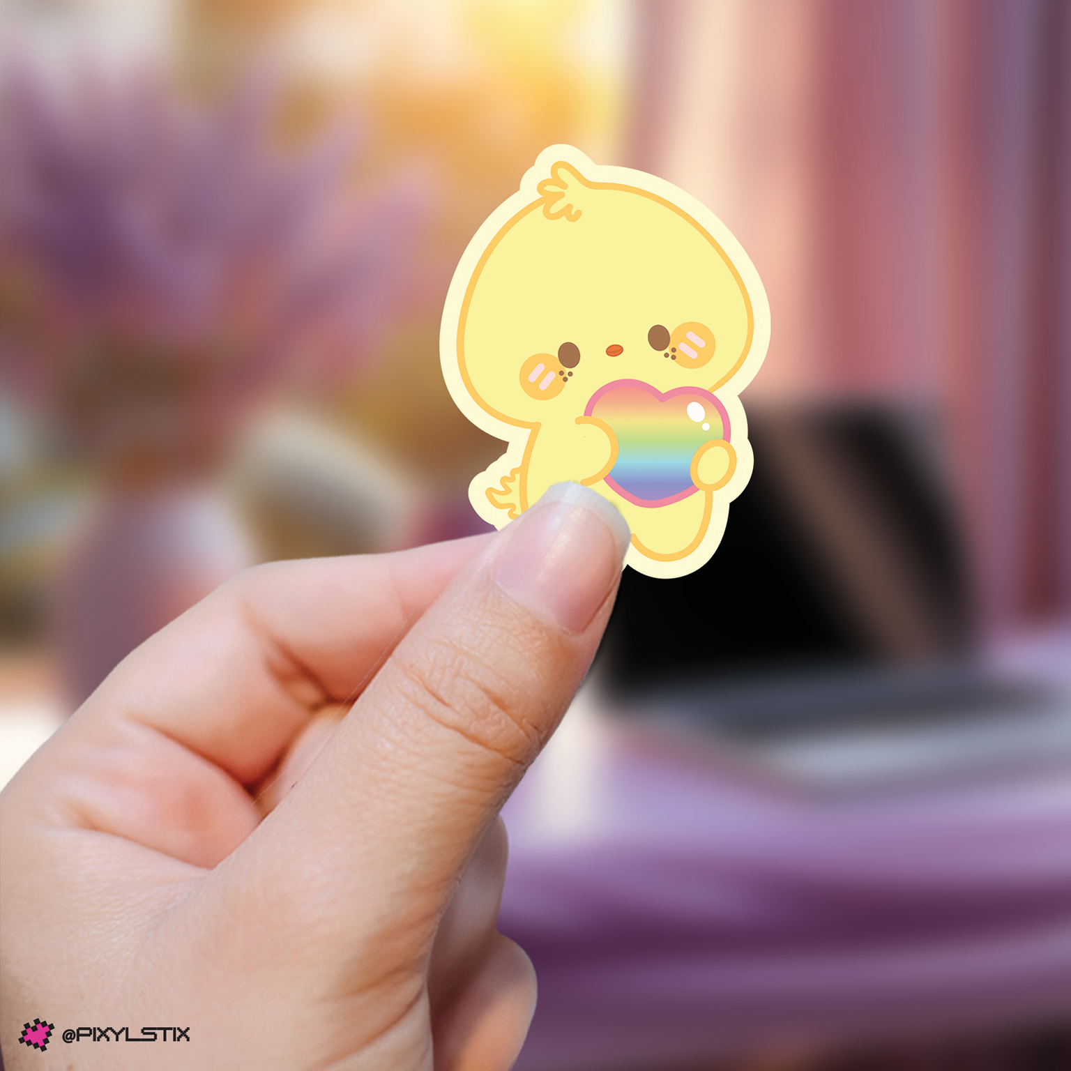 Hand holding a felix skzoo sticker with a rainbow heart against a blurred background