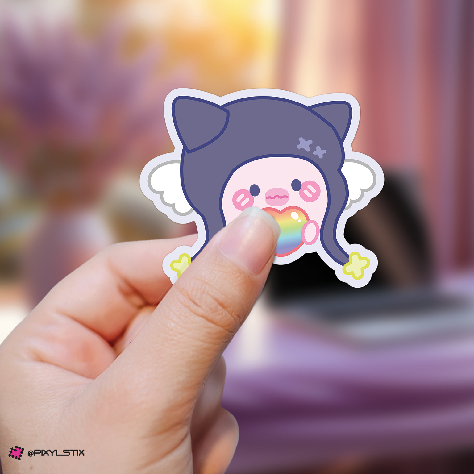 Hand holding a gaon xdinary monsters sticker with a rainbow heart against a blurred background