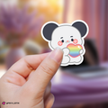 Hand holding a gunil xdinary monsters sticker with a rainbow heart against a blurred background