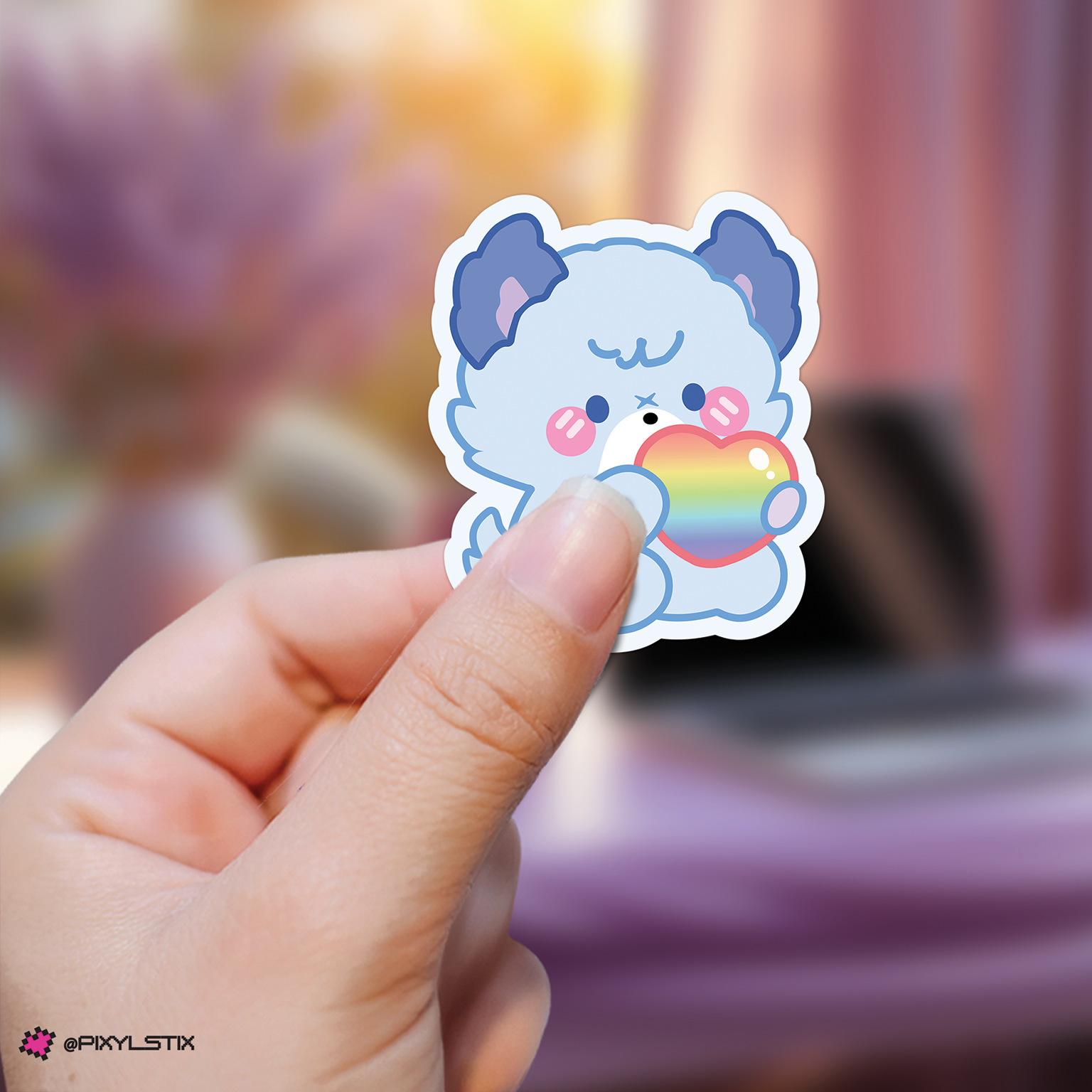 Hand holding a jooyeon xdinary monsters sticker with a rainbow heart against a blurred background