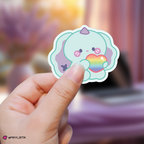Hand holding a junhan xdinary monsters sticker with a rainbow heart against a blurred background
