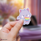 Hand holding a san aniteez sticker with a rainbow heart against a blurred background