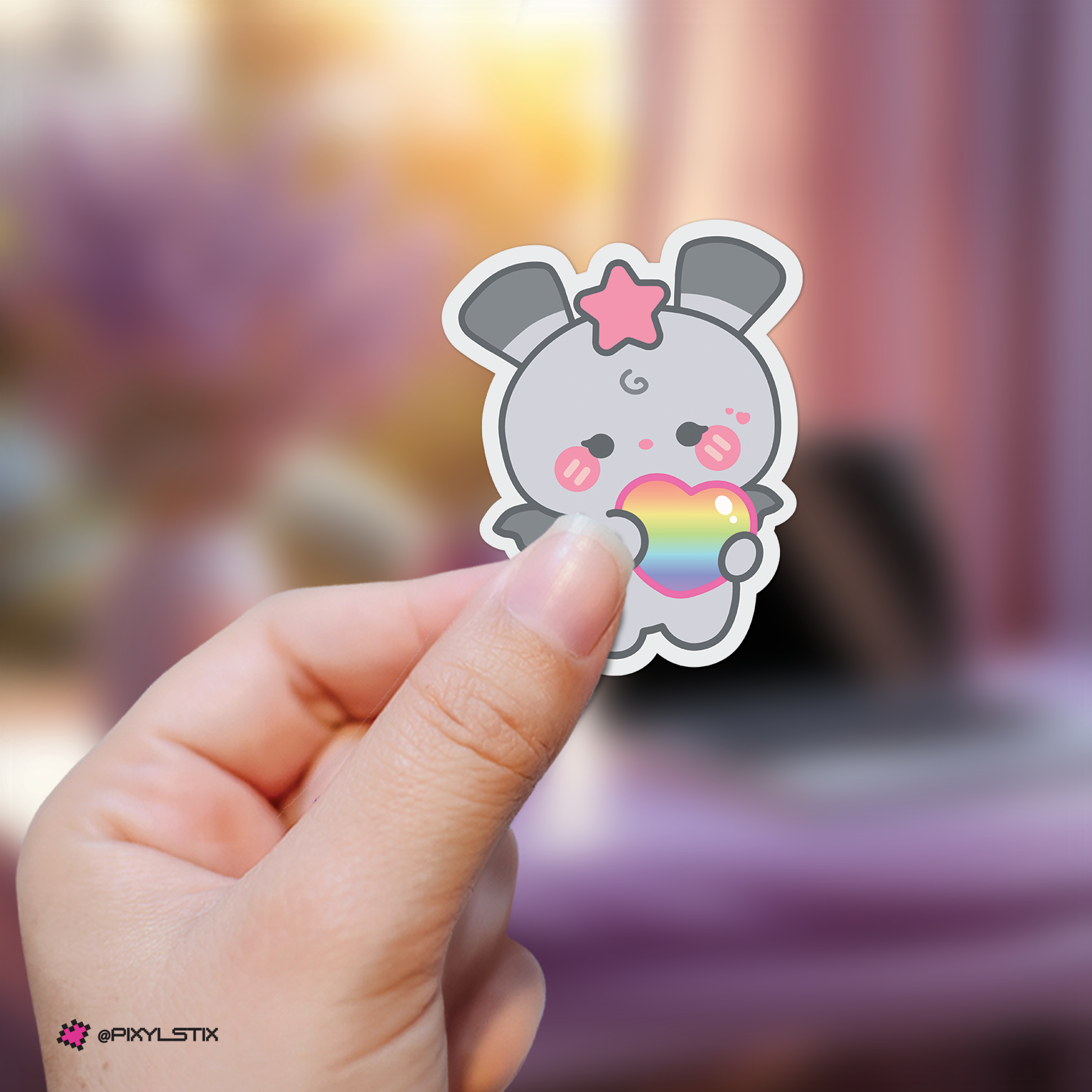Hand holding a seonghwa mighteez sticker with a rainbow heart against a blurred background