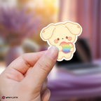 Hand holding a yunho aniteez sticker with a rainbow heart against a blurred background