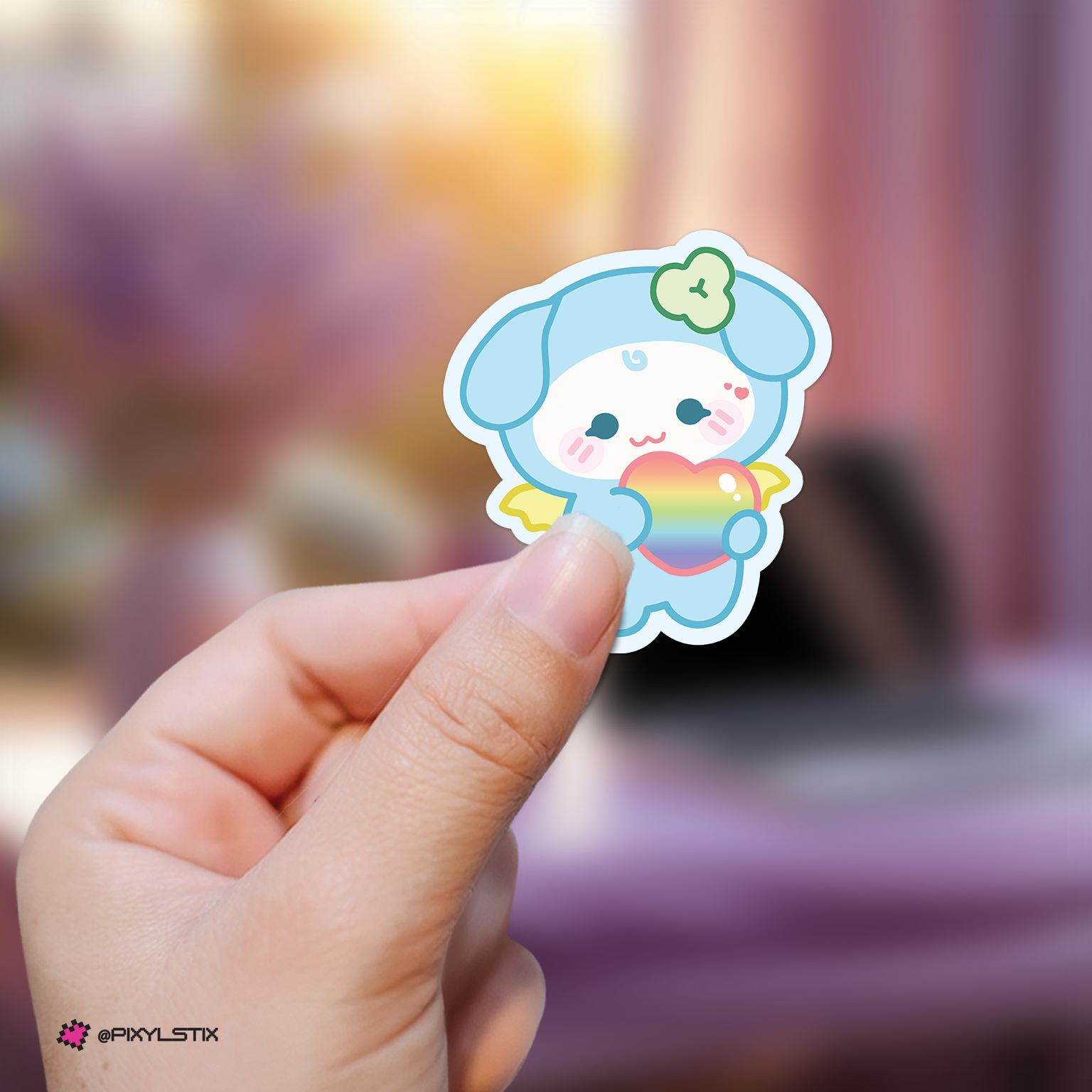 Hand holding a yunho mighteez sticker with a rainbow heart against a blurred background