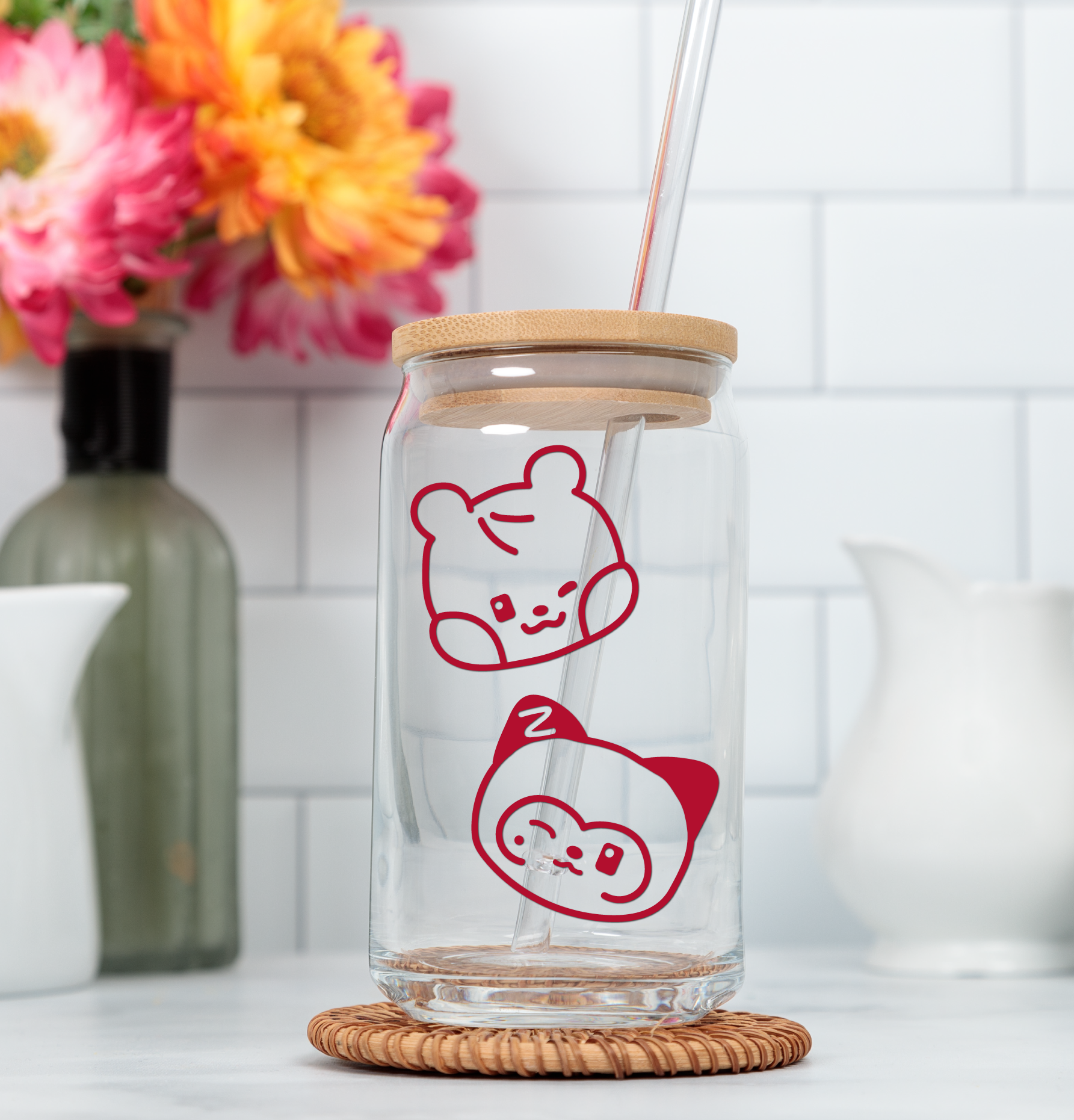 Clear glass tumbler with wooden lid and zeroni illustrations on a white surface with flowers in the background.