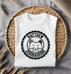 White t-shirt with a black decal placed on a woven mat with dried plants.