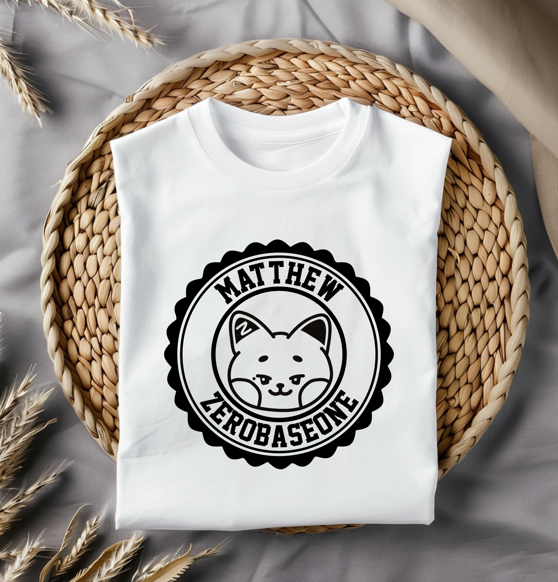 White t-shirt with a black decal placed on a woven mat with dried plants.