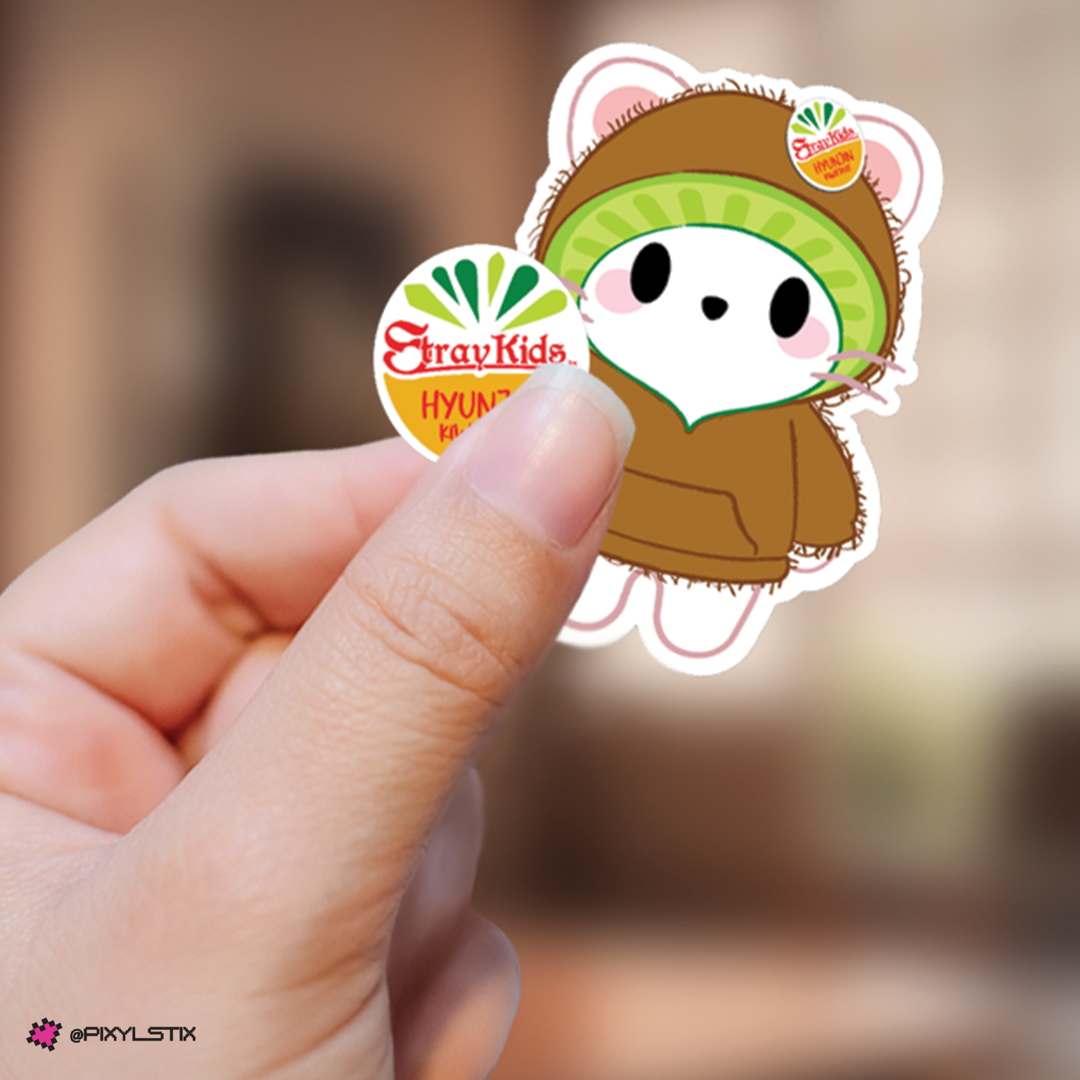 A hand holding a jiniret sticker wearing a brown hoodie and kiwi colored hood plus a circular fruit sticker.