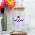 Clear glass tumbler with mighteez deecal, wooden lid, and straw on a white surface with flowers in the background.