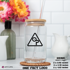 Clear glass tumbler with wooden lid and straw on a white surface with flowers in the background
