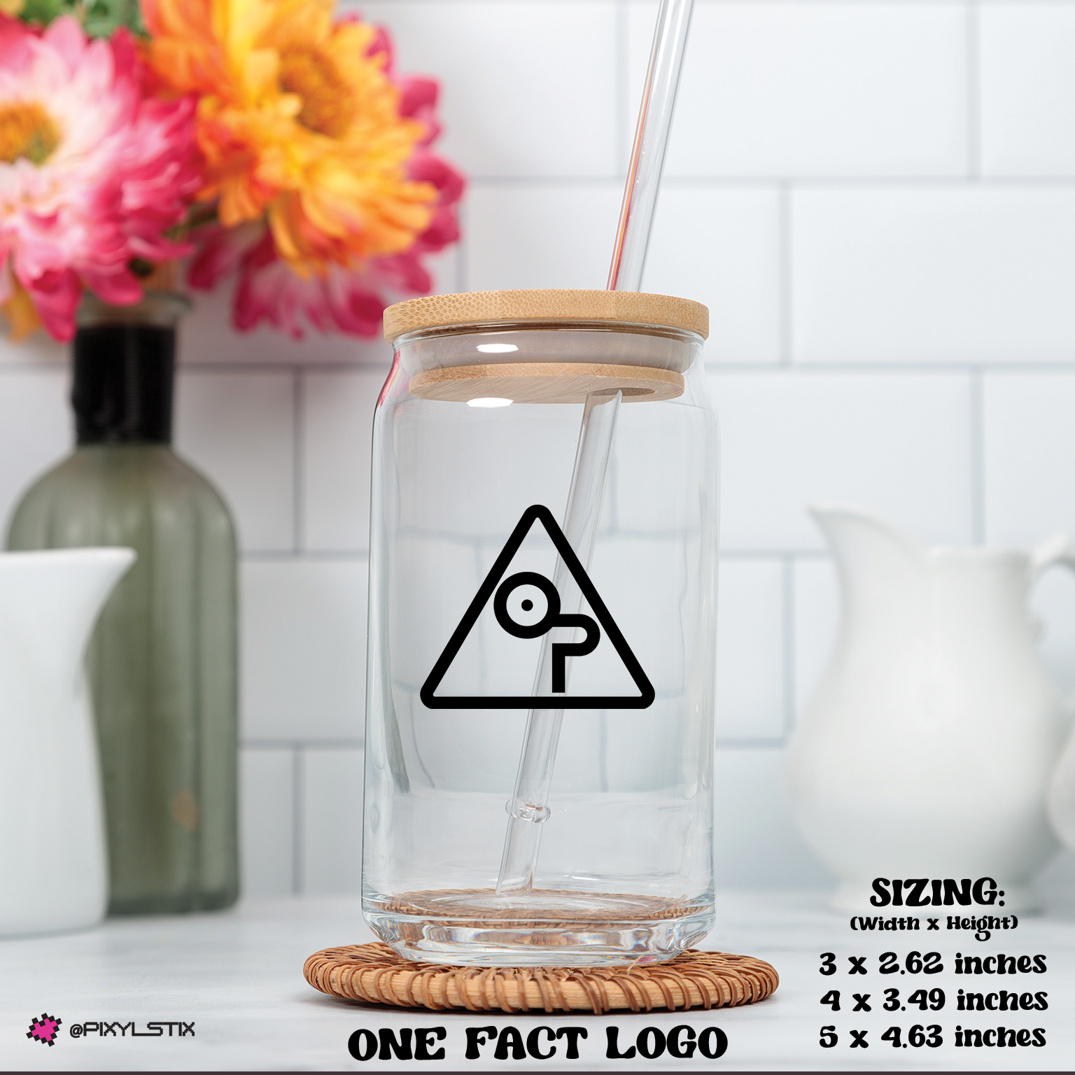Clear glass tumbler with wooden lid and straw on a white surface with flowers in the background