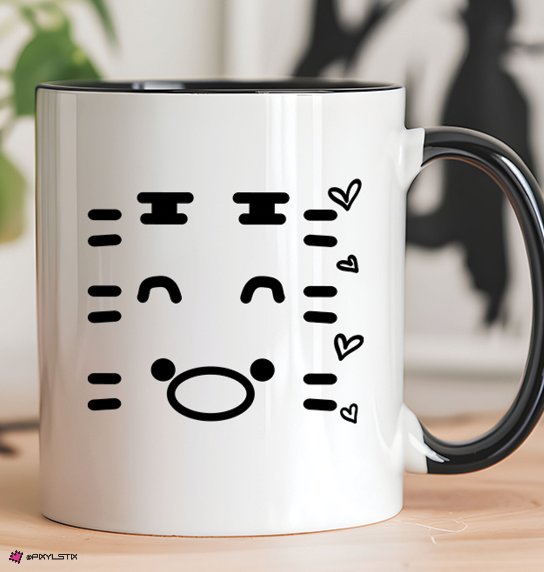A white ceramic coffee mug with a black handle and black interior, featuring a black miniteen face decal on the front, set on a light wooden surface with a blurred background.