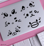 A set of black xdinary monster face decals displayed on the back of a silver laptop, resting on a pink textured mat with a white keyboard partially visible in the corner.