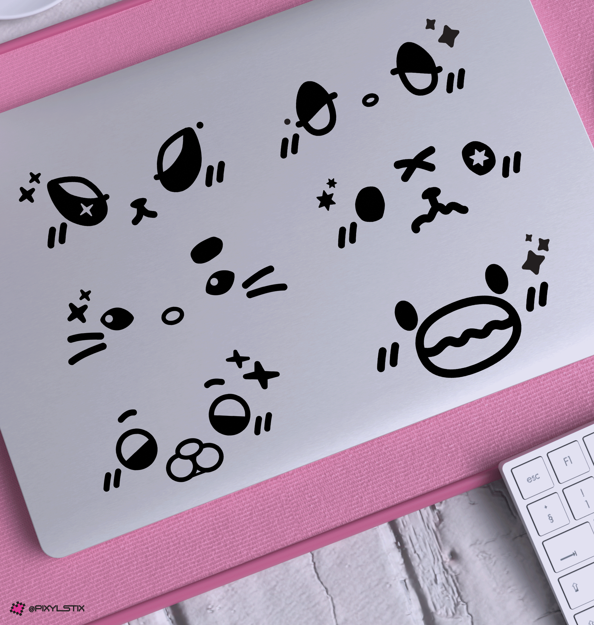 A set of black xdinary monster face decals displayed on the back of a silver laptop, resting on a pink textured mat with a white keyboard partially visible in the corner.