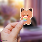 Hand holding a zeroni matthew sticker with a rainbow heart against a blurred background